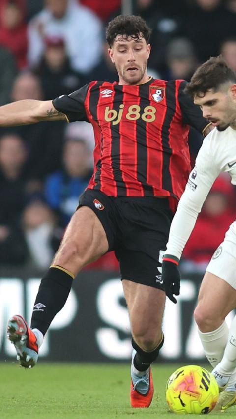 Marcos Senesi wears full AFC Bournemouth kit and goes to tackle another player who has a yellow ball.