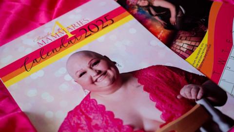 The front cover of the thanks for the mammaries calendar shows a woman with no hair wearing a pink lace top and smiling at the camera