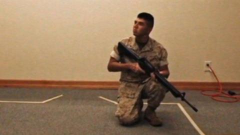 A man wearing camouflage clothing is kneeling on the floor holding a large gun.