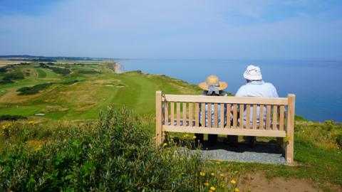 Two people sat on a bench on a cliff top at Sheringham looking out to sea