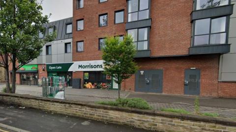 A building block set back from the road side with the Morrisons store on the ground floor.