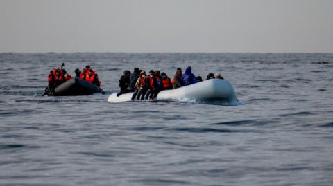 An inflatable boat packed with people wearing orange life jackets.