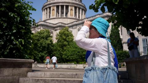 A woman wearing a long sleeved white blouse and turquoise hat shields her face from the sun