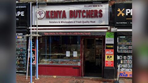The shopfront of Kenya Butchers, which has a maroon shopfront with a large window. 
