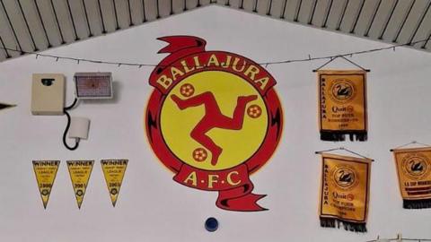 A shot of a large emblem, representing Ballajora AFC. It is visually very similar to the Manx national crest