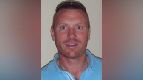 Christopher Chittock wearing a blue top with sunglasses on top of his head, he has very short hair. 