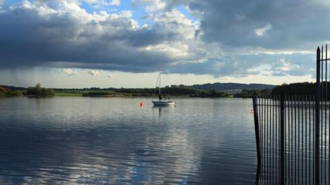 A still loch with a sailing boat in the middle of it