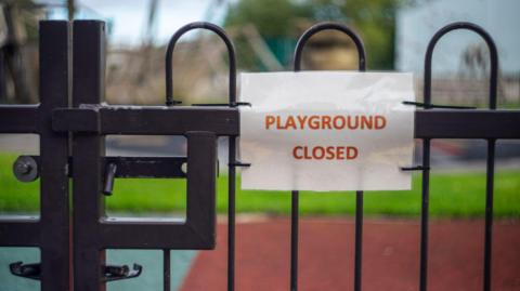 A playground gate with a sign attached which says "PLAYGROUND CLOSED"