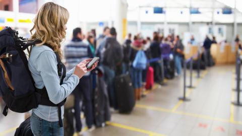 Female traveller texting at airport check-in desk - stock photo