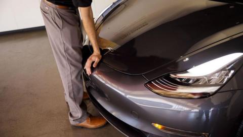 A person closes the hood of a Tesla