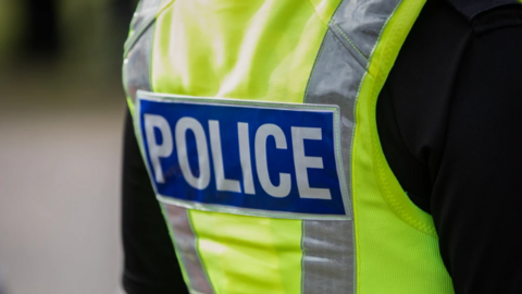 A police officer stands with his back to the camera with his fluorescent jacket showing the "police" label. 
