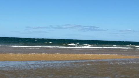 An empty stretch of the sandy beach at Redcar looking to the sea which is slighty frothed up by the waves. There is water pooled on the sand further inland.