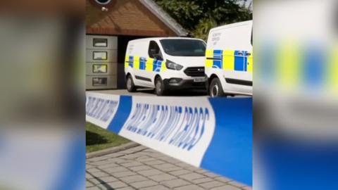 Police forensic vans behind crime scene tape at a residential property