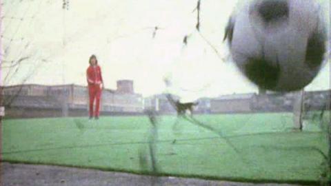 Peter Purves kicking a football into a goal on the artificial pitch.