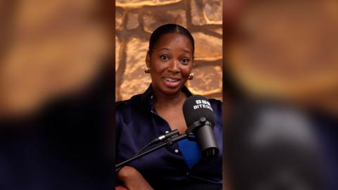 Jamelia looks at the camera. She's wearing a navy shirt that's unbuttoned and has a surprised expression.