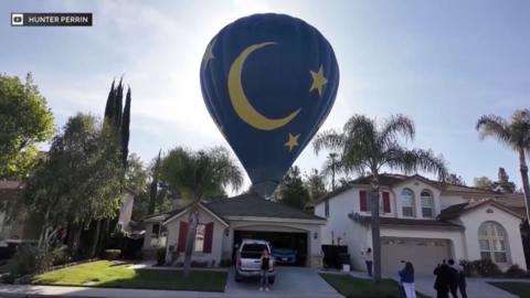 A blue hot air balloon lands in a backyard.