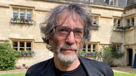 Neil Gaiman wearing a black t-shirt and black jacket