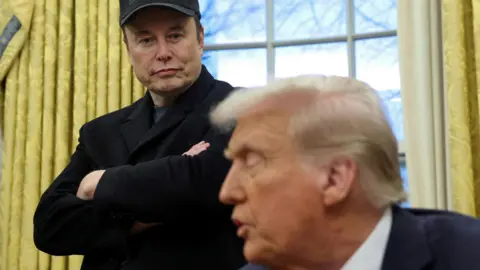 Elon Musk listens to U.S. President Donald Trump speak in the Oval Office of the White House in Washington