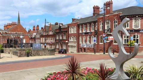 Stock image of Rotherham's town, with an array of different buildings in a row and a metal statue