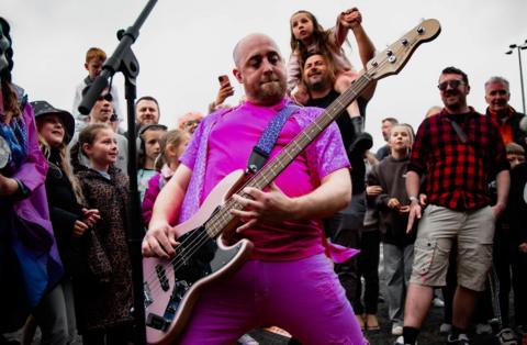 A man in a pink T-shirt plays an electric guitar in the middle of a crowd at the Good Times Festival in Bristol