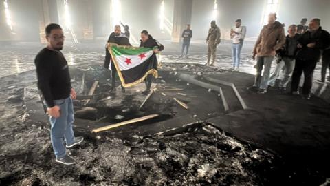 Rebel fighters stand next to the burning gravesite of Syria's late president Hafez al-Assad at his mausoleum