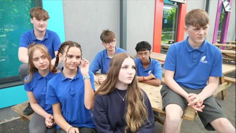 A group of teenagers sitting on a bench outside in the school premises