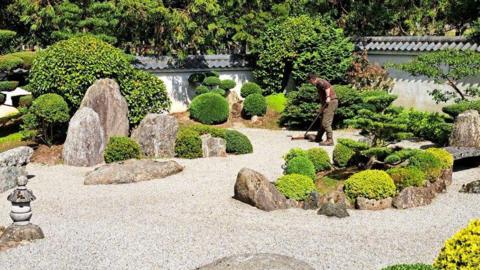A karesansui "dry garden", enclosed by a white walls. Gravel is arranged in circular and curved shapes representing water, and small ornamental trees are set around rocks.