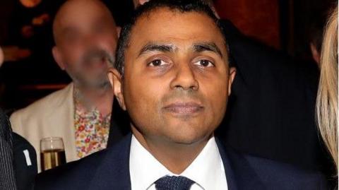 Lord Waheed Alli poses for a photo at an event, wearing a blue suit