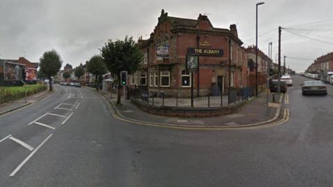 A Google street view image of a road junction with a pub at its corner. The pub sign, The Albany, is written on gold lettering on the red-bricked building and the sign has a portrait of a man in regency clothing. Other buildings can be seen in the two streets going away from the junction.