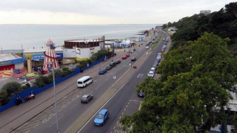 The seafront at Southend-on-Sea with an adjacent funfair and tree-lined road.