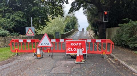 Closed road signs block a route leading towards a bridge. 