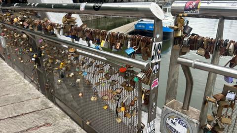 Hundreds of padlocks, most which are rusty, locked onto the metal railing of a bridge in Bristol's harbourside