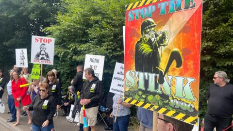 People protesting at the side of the road about Walleys Quarry landfill. Some are holding signs that say "stop the stink".