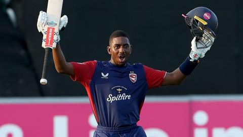 Tawanda Muyeye raises his helmet and bat in each arm in celebration