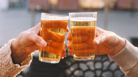 Two people clinking beer glasses outdoors 