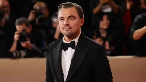 eonardo DiCaprio wears a black tuxedo as he poses on the red carpet at the Golden Globes in Beverly Hill