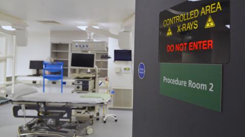 View through an open door - which carries a warning about x-rays - to a hospital room with a specialist bed and a number of computer monitors