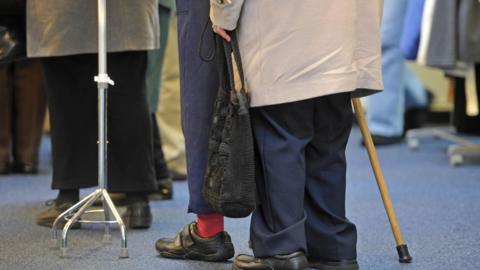 A general view of elderly people. There is a walking stick and a walking frame. 