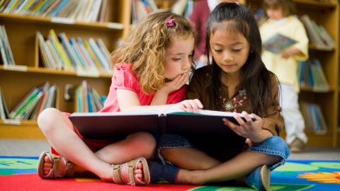 Llun dwy ferch yn darllen llyfr yn llyfrgell