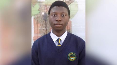 Matt is looking at the camera, it is a school photo. He is wearing a navy blue school jumper and shirt and tie underneath.