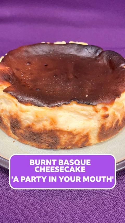 A vanilla cheesecake with a burnt brown top sits on a white board against a purple background