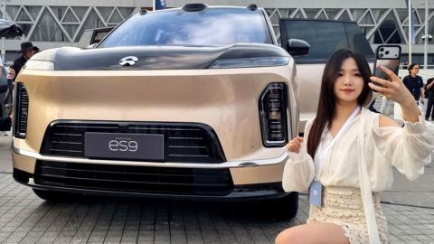 A woman uses her phone near NIO's new flagship electric SUV ES9, displayed ahead of the car's launch event, in Beijing, China 27 May, 2026.