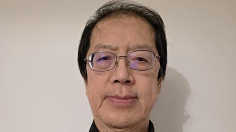 This is a head shot of Joe Wong who is looking at the camera. He is standing in front a white wall.