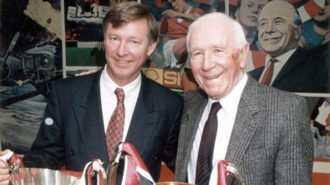 Sir Alex Ferguson and Matt Busby pose with trophies won by Manchester United