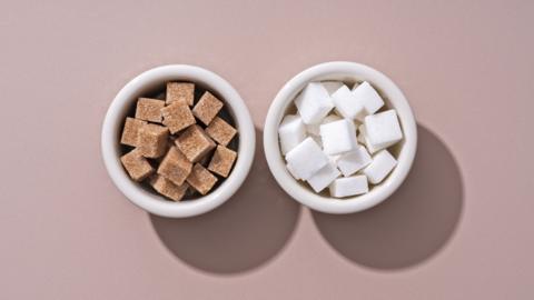 Two small bowls of sugar cubes next to each other, one containing brown sugar cubes, the other containing white sugar cubes. 