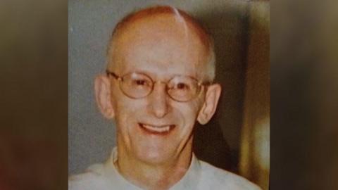 A close-up picture of Paul Adams smiling on his wedding day. He had very short grey hair and wore round glasses and a white smart shirt.