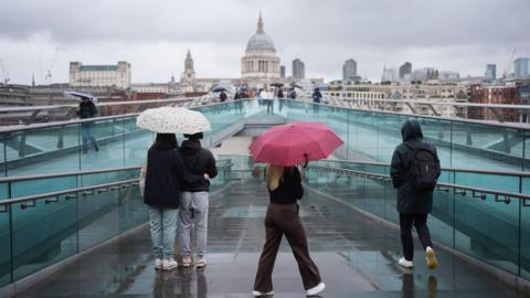 People with umbrellas walking along the Millennium Bridge, in London, during a rain shower