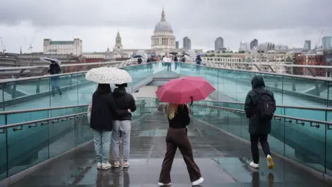 People with umbrellas walking along the Millennium Bridge, in London, during a rain shower