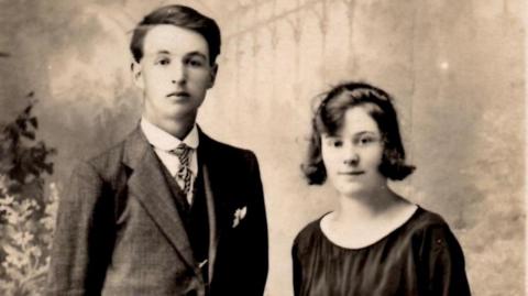 A black and white photograph showing a man with very dark hair wearing a suit, and a woman with dark hair down to her chin wearing a black blouse.