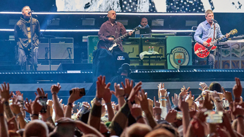 Fans wave their hands above their heads as Oasis perform on stage